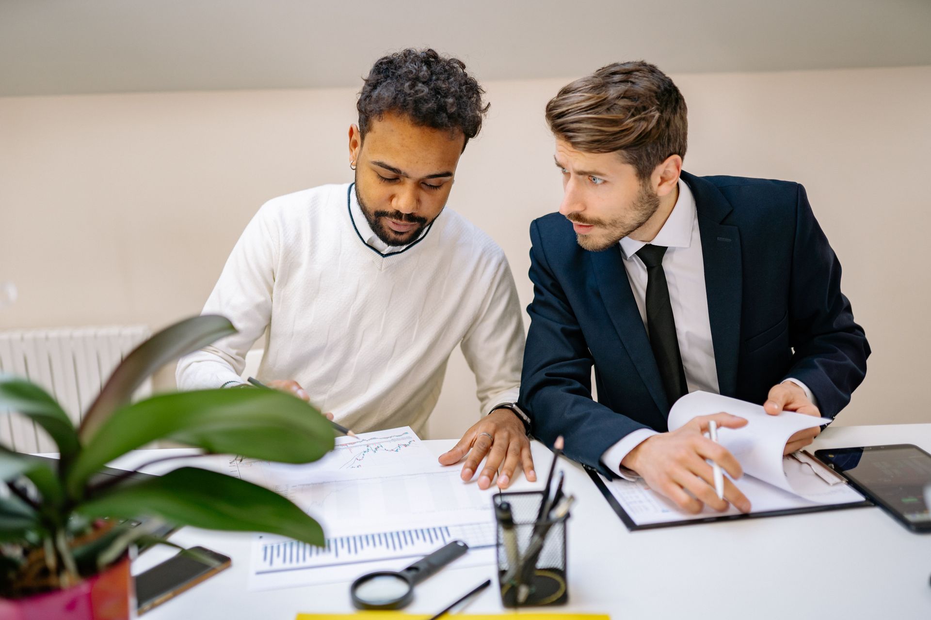 Two coworkers review documents at a desk, pointing at papers in a bright office.