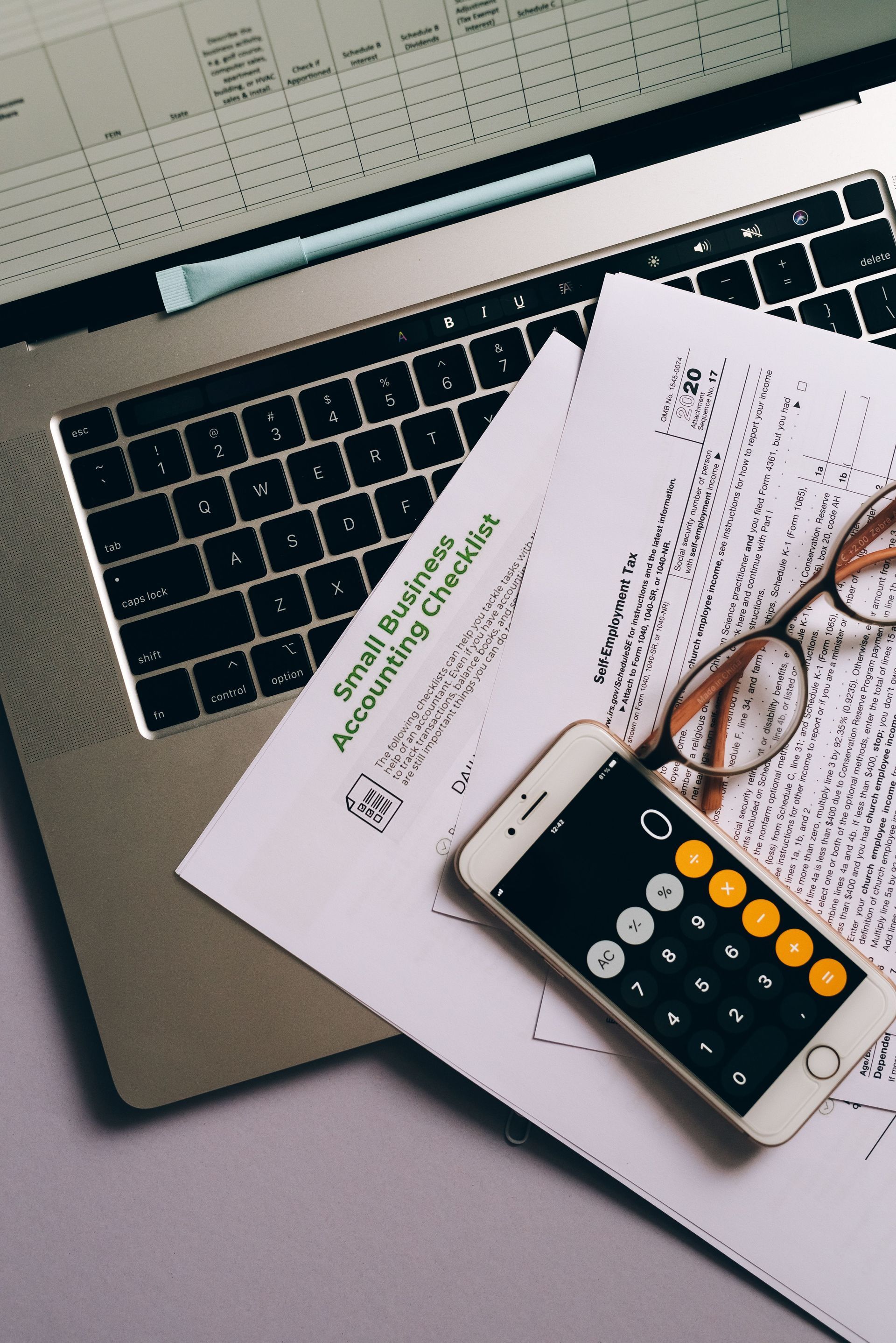 Calculator, glasses, and papers on a laptop keyboard in a workspace.