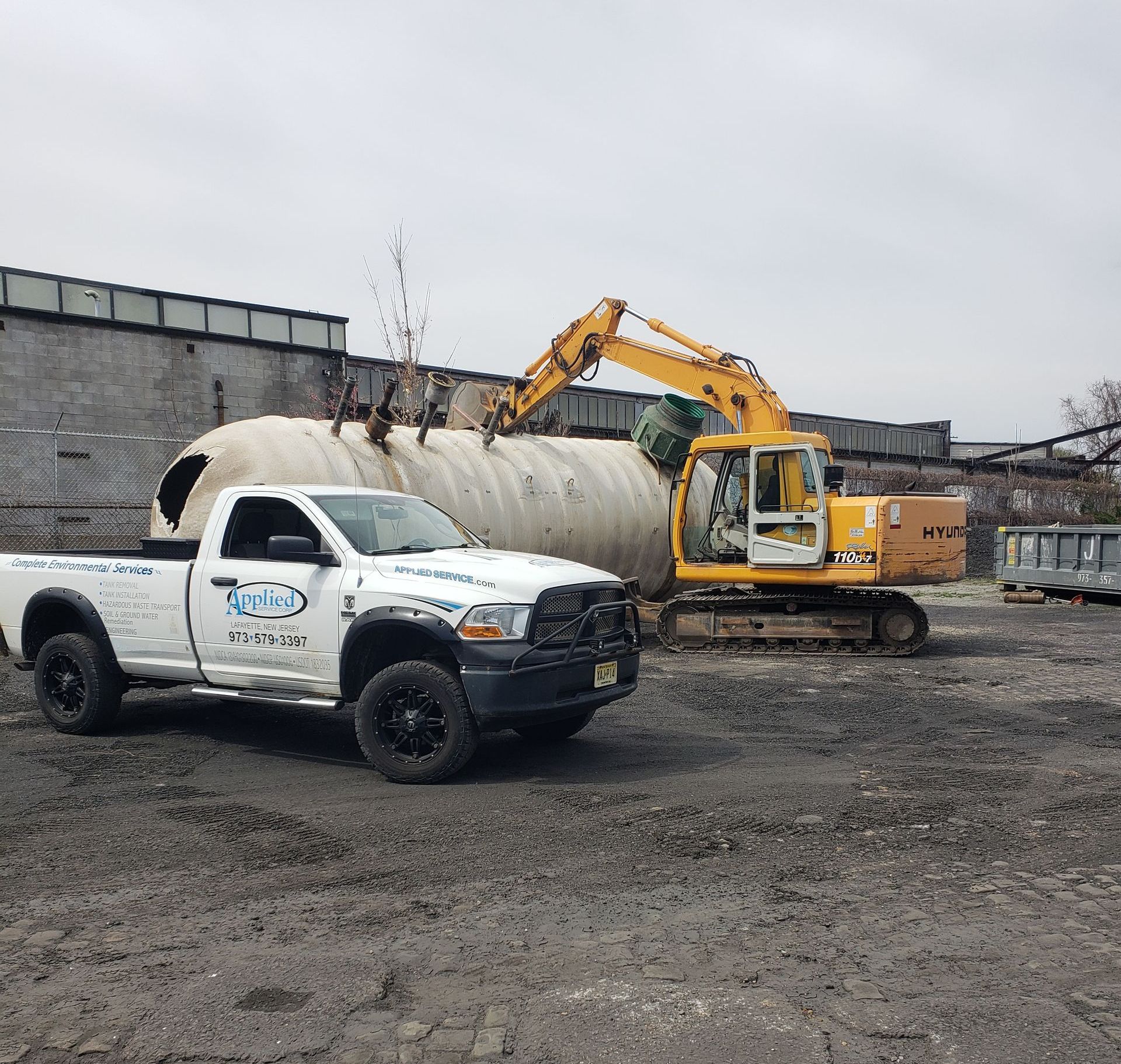 White pickup truck, yellow excavator, and large concrete structure at a construction site on an overcast day.
