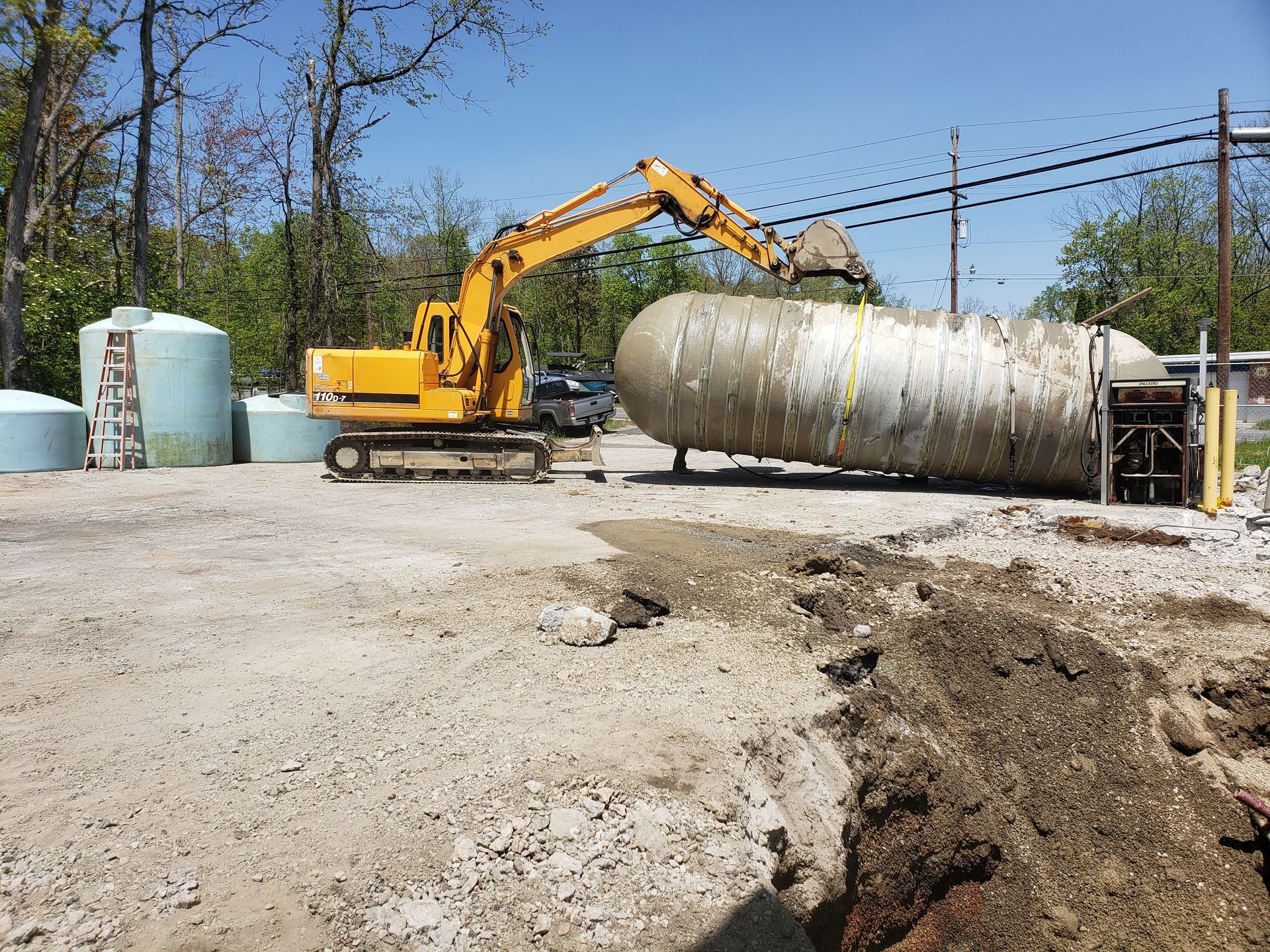 A yellow excavator is digging a hole in front of a large propane tank.