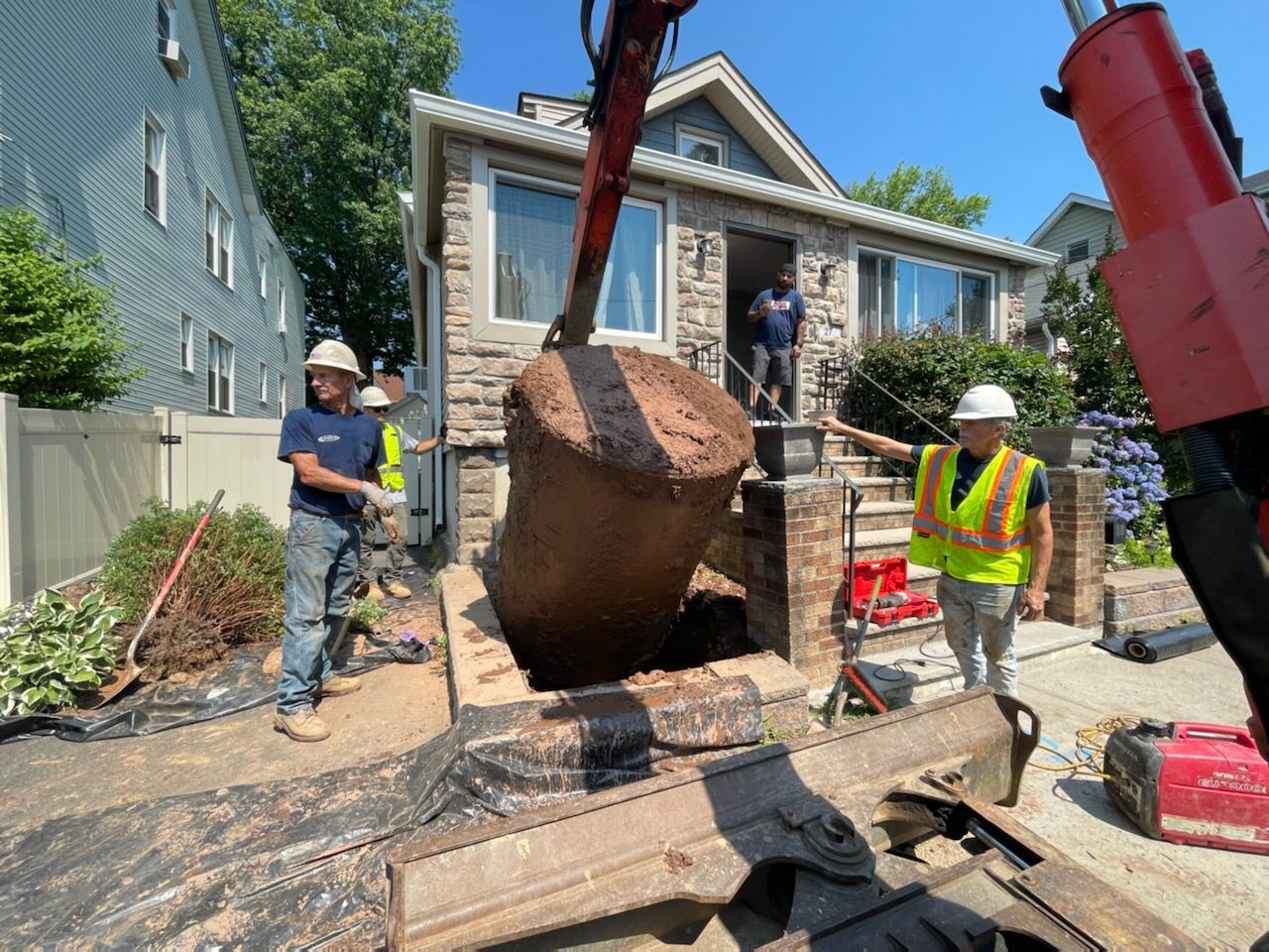 A group of construction workers are working on a large rock in front of a house.