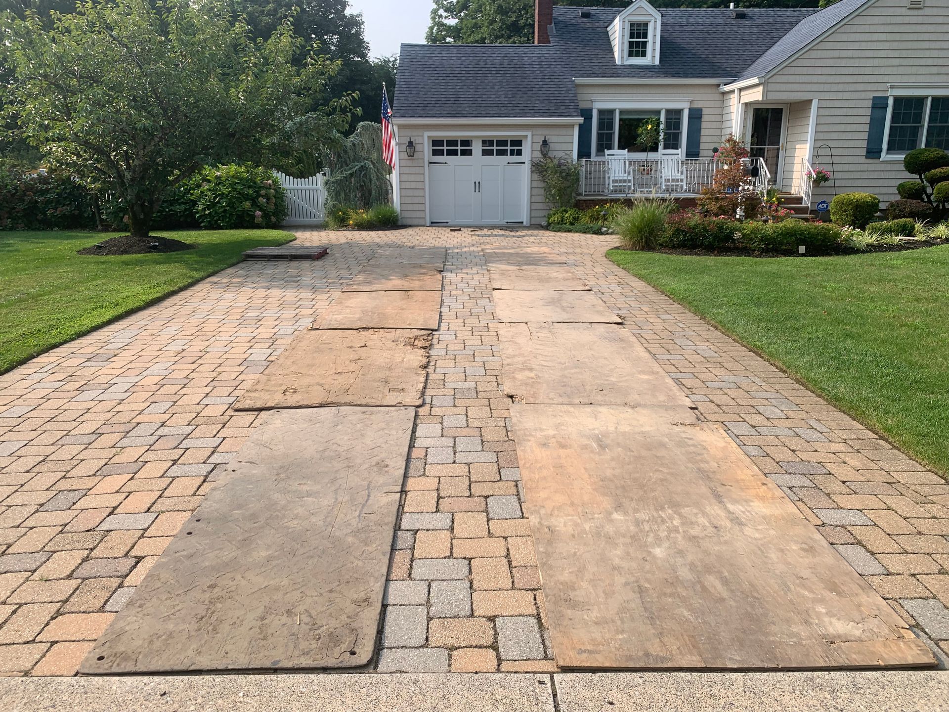 Driveway with large, square concrete slabs surrounded by brick pavers leading to a white house with a garage.