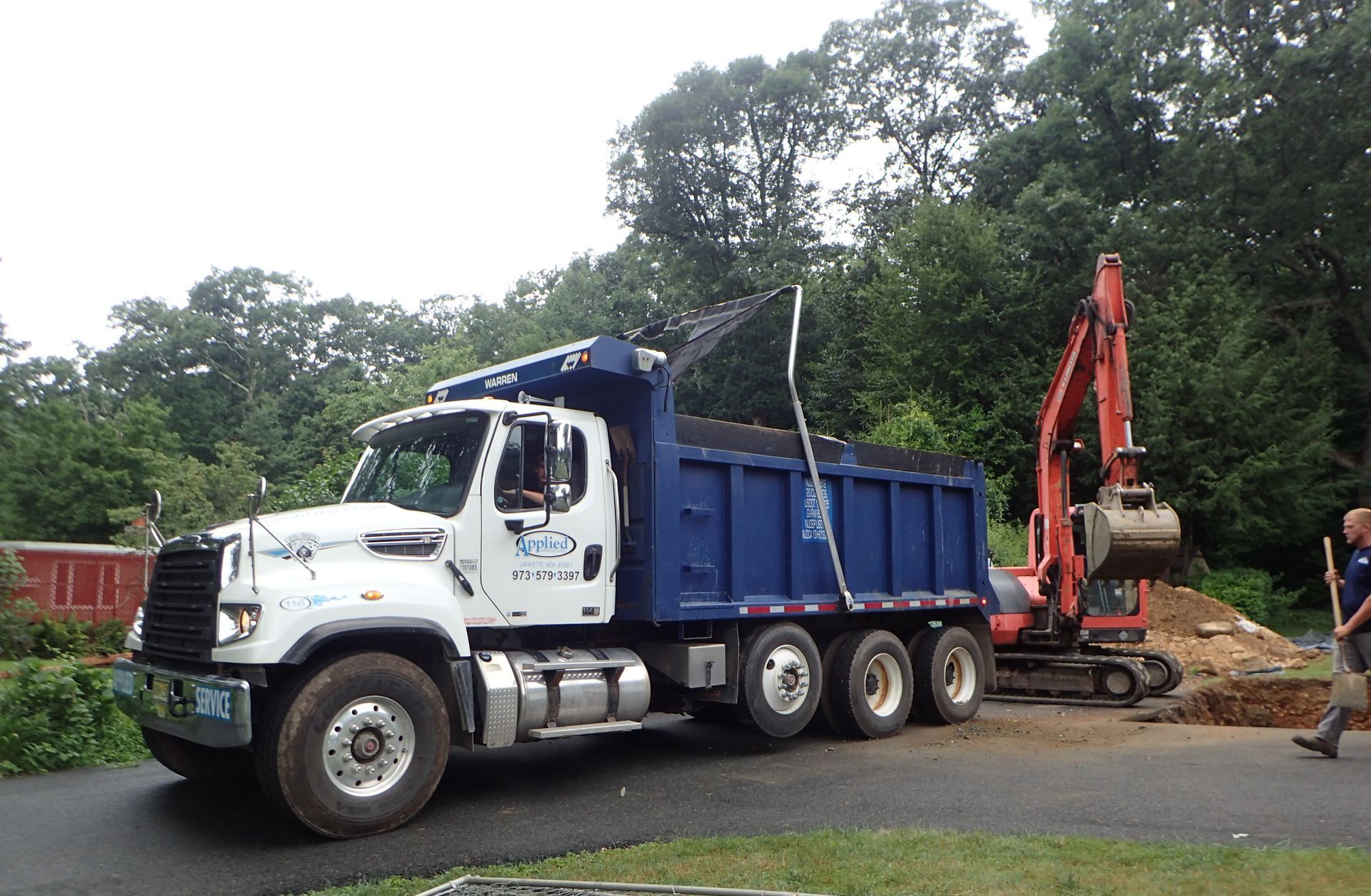 A white and blue dump truck is parked on the side of the road