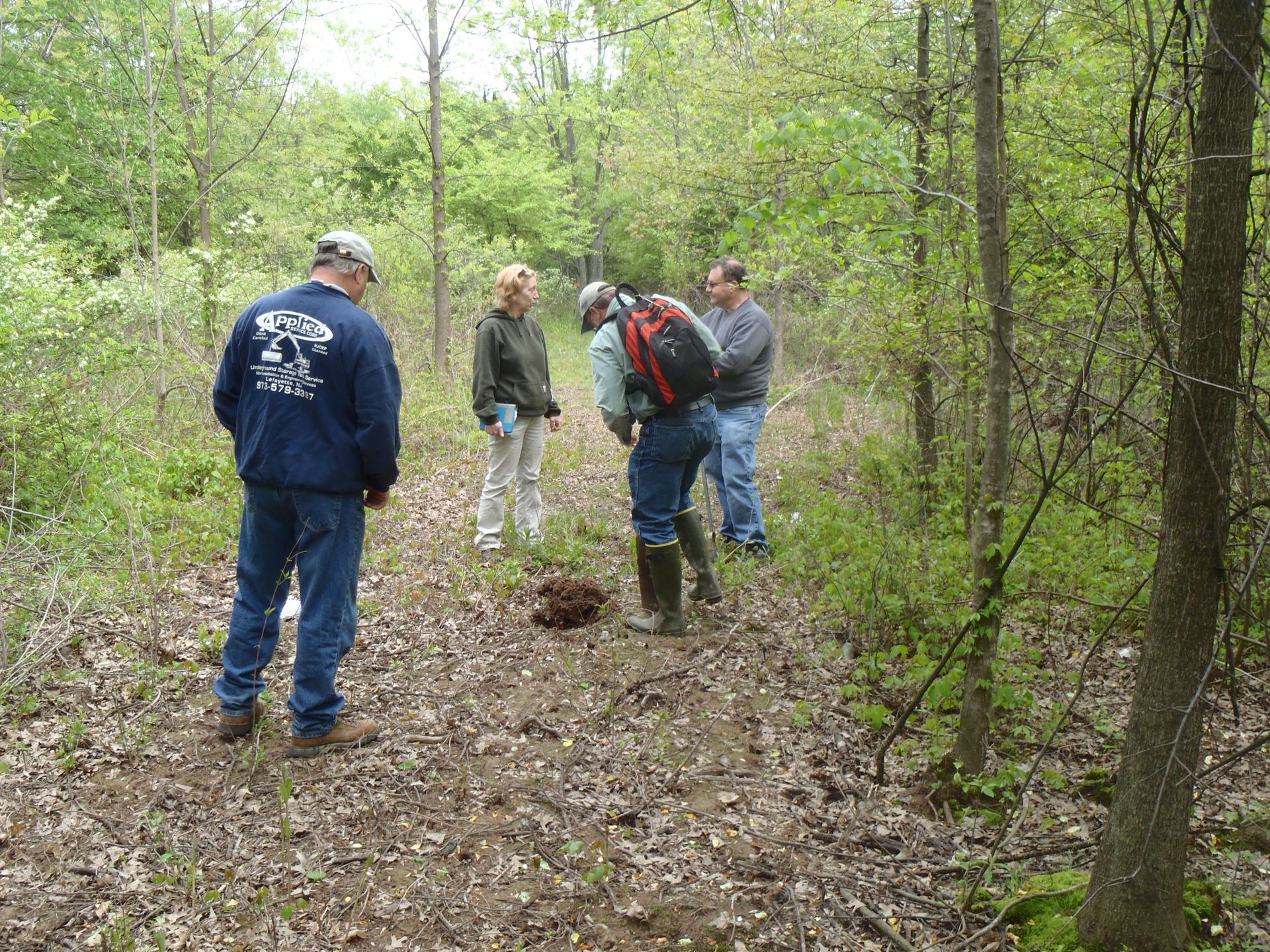 Four people examining a small pile of something brown in a wooded area.