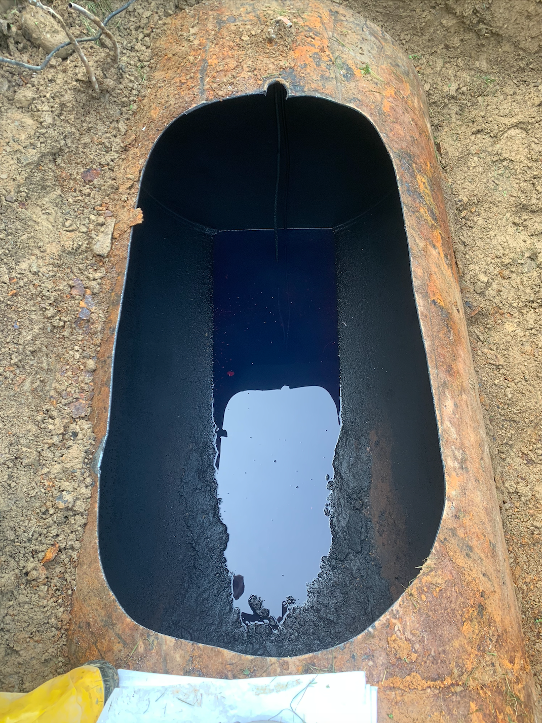 A rusty metal container cut open, filled with dark liquid reflecting the sky.