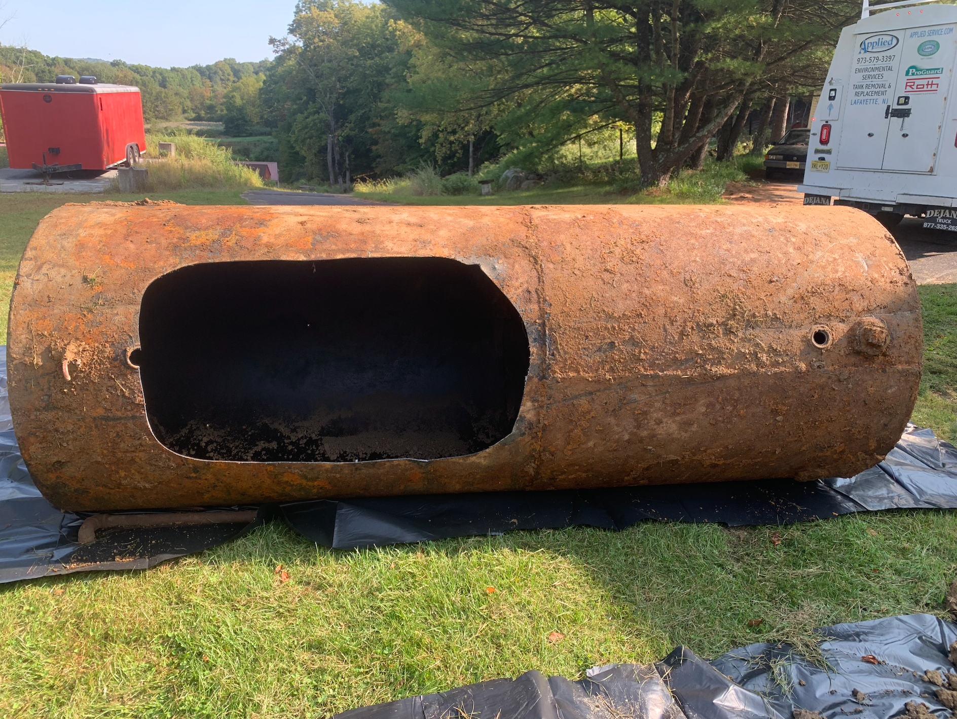 Rusty, cylindrical metal tank with a large cut-out on green grass.