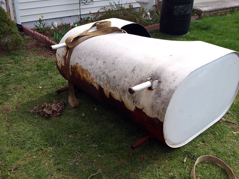 A large white tank is sitting on the grass in front of a house.