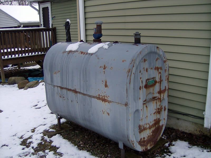 A rusty metal tank is sitting in the snow in front of a house