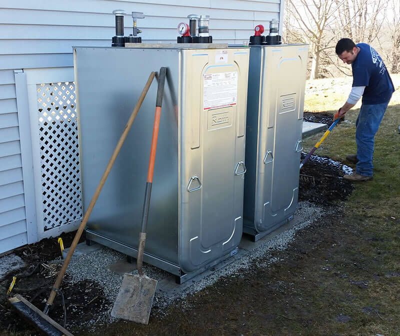 Man shovels soil around two new, silver oil tanks installed next to a house.