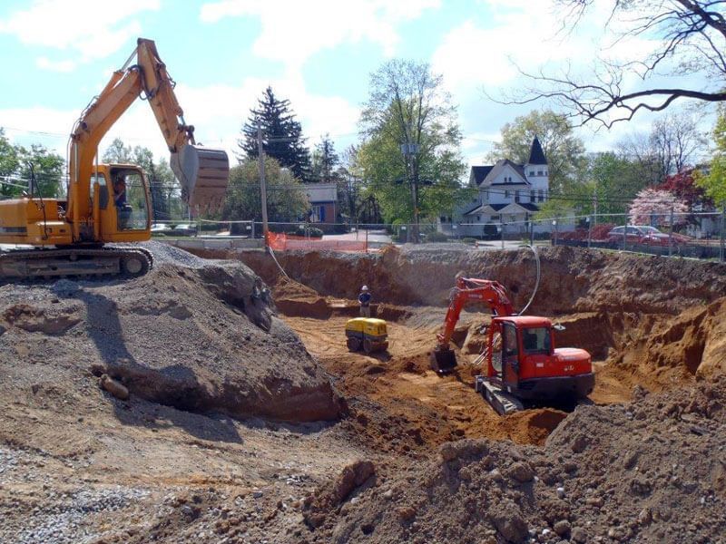 Construction site with excavators digging; houses in background.