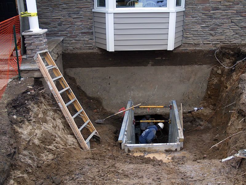 A man is working in a hole in front of a house.