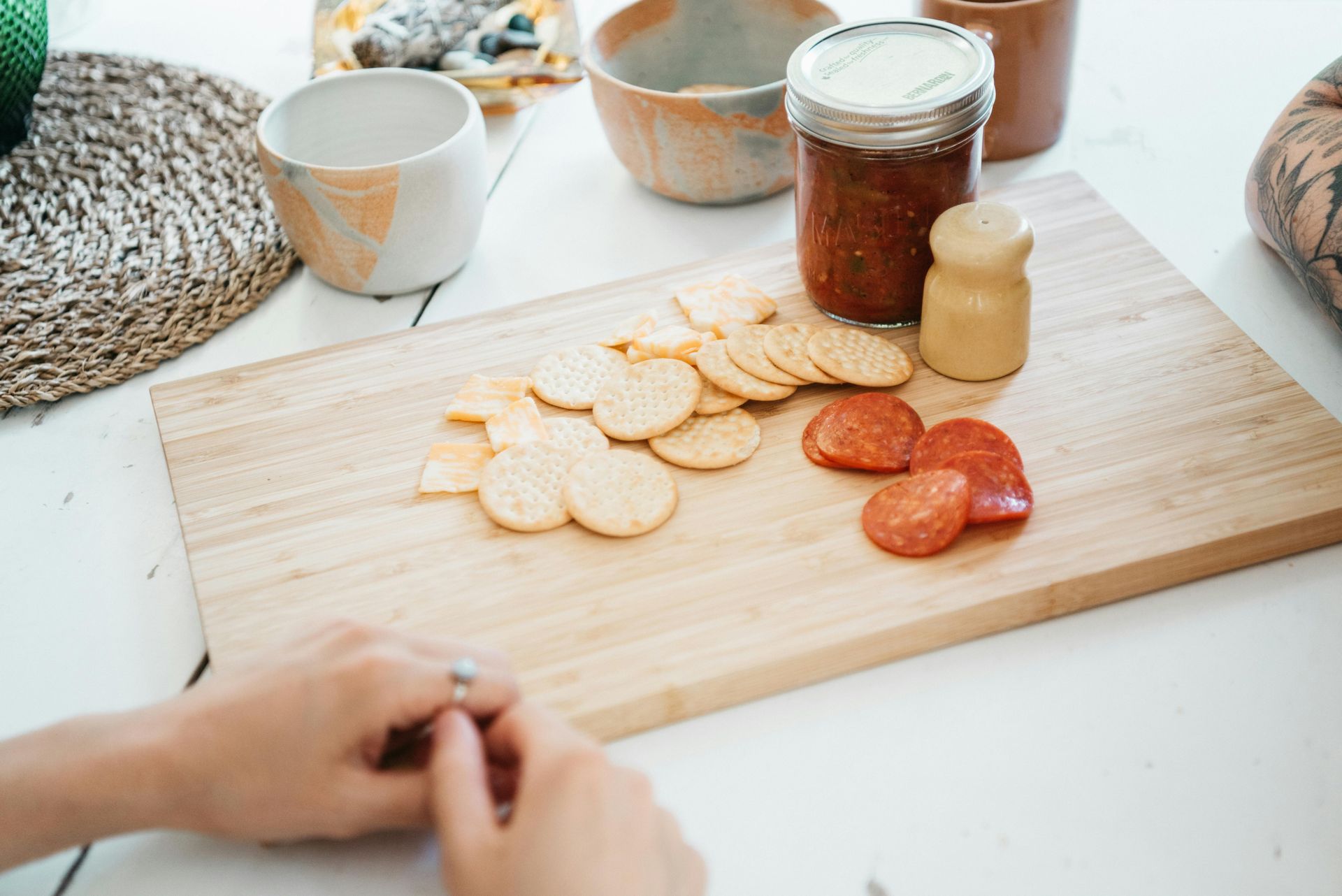Una persona está cortando galletas y pepperoni en una tabla de cortar de madera.
