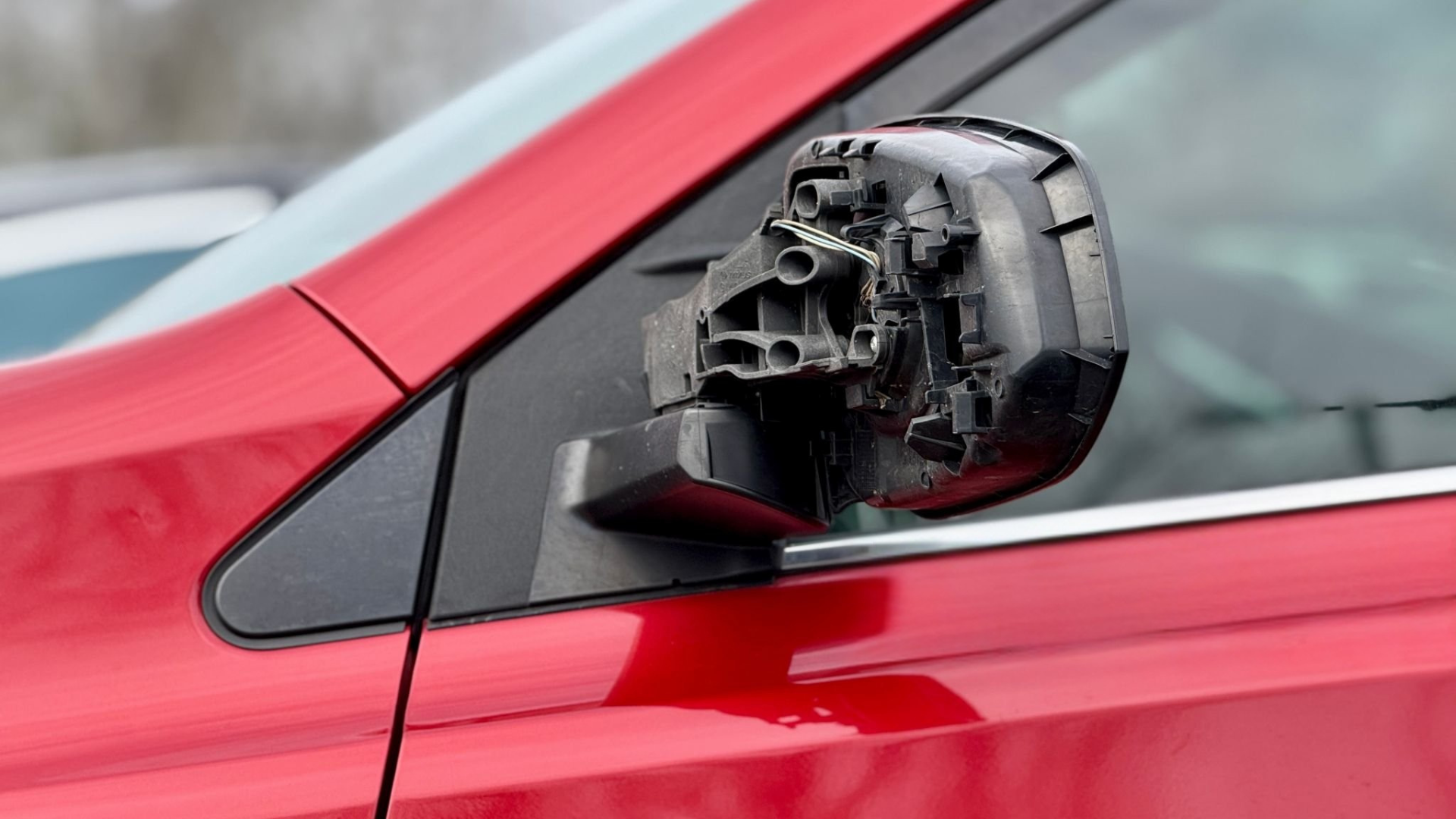 Damaged red car side mirror, showing broken plastic housing and exposed components.