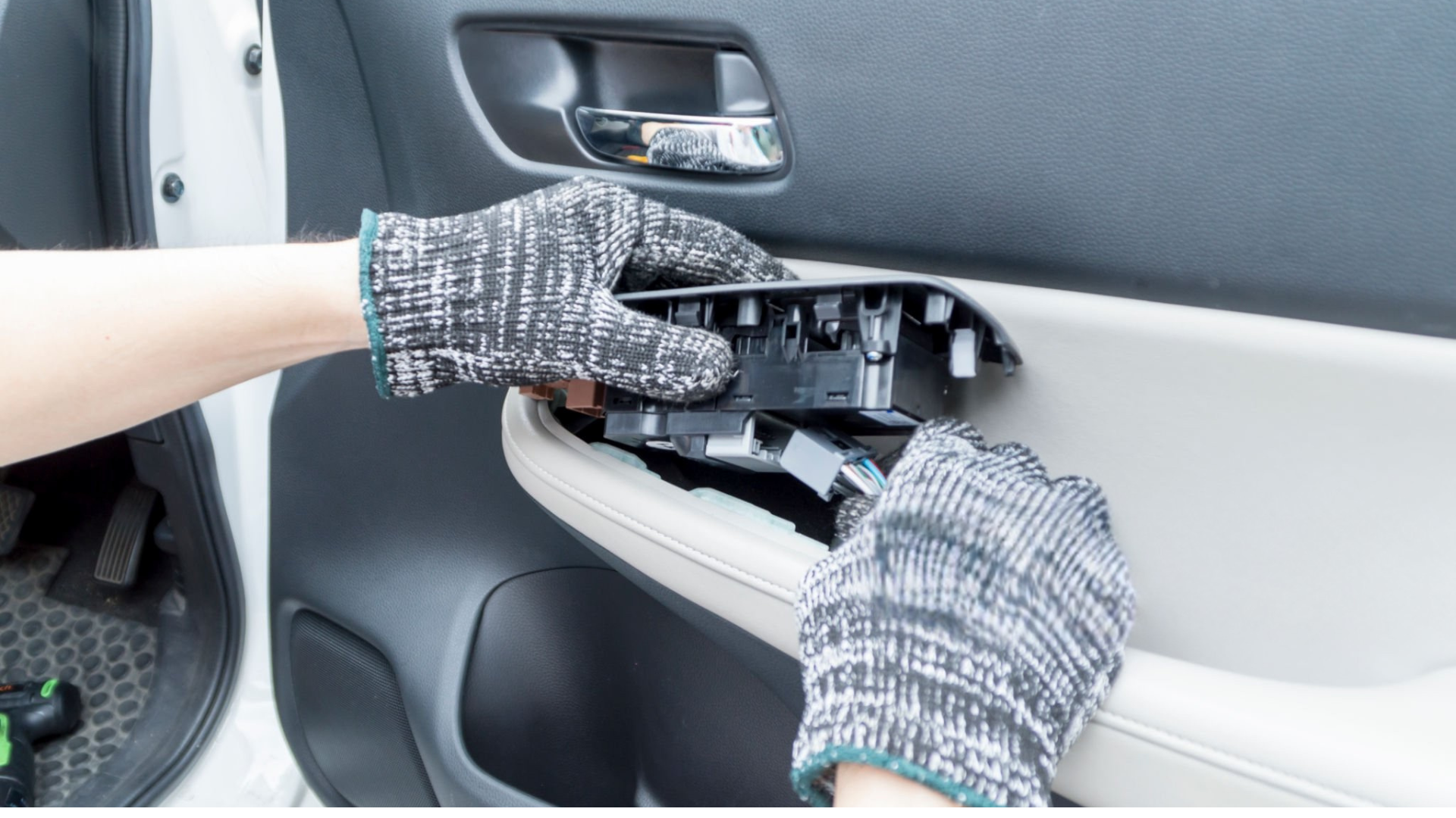Hands wearing gloves removing the interior door handle of a white car.