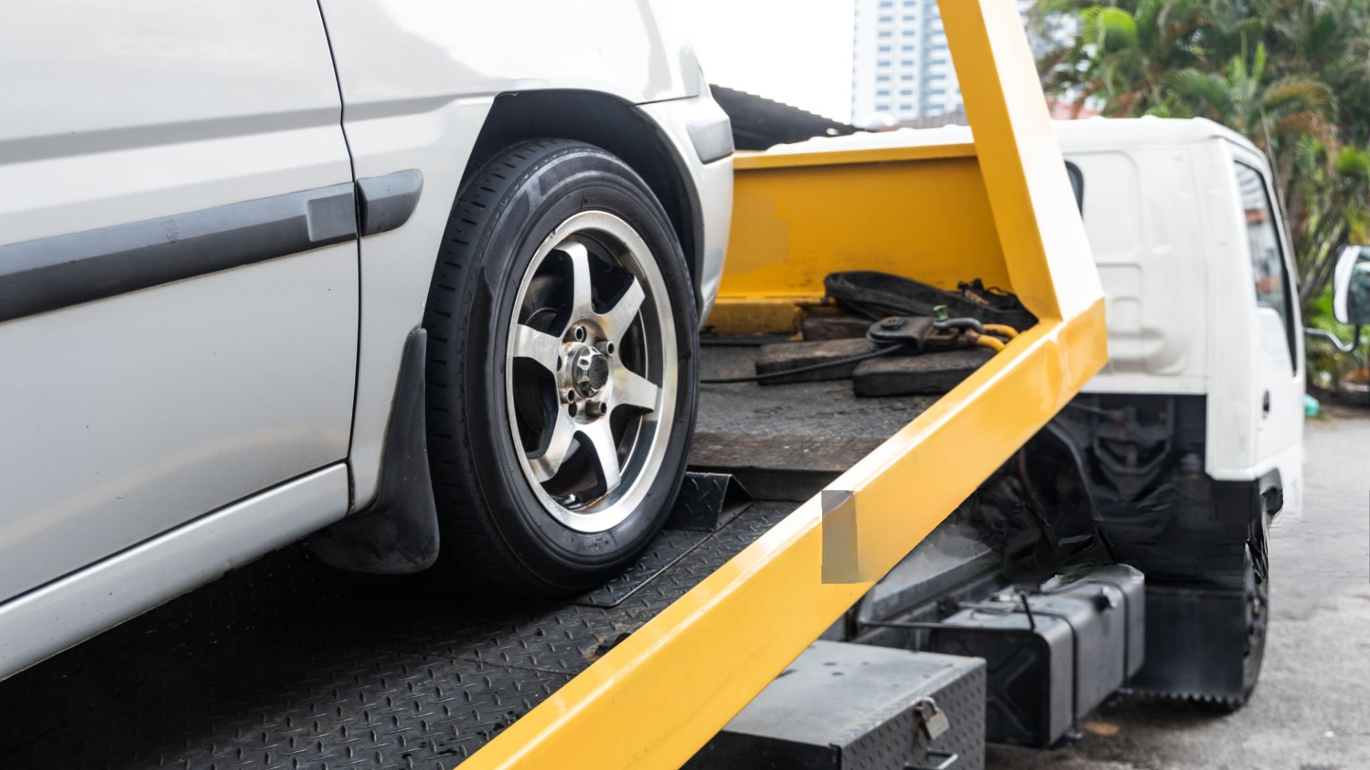 White car being loaded onto a yellow and black tow truck on a wet street.