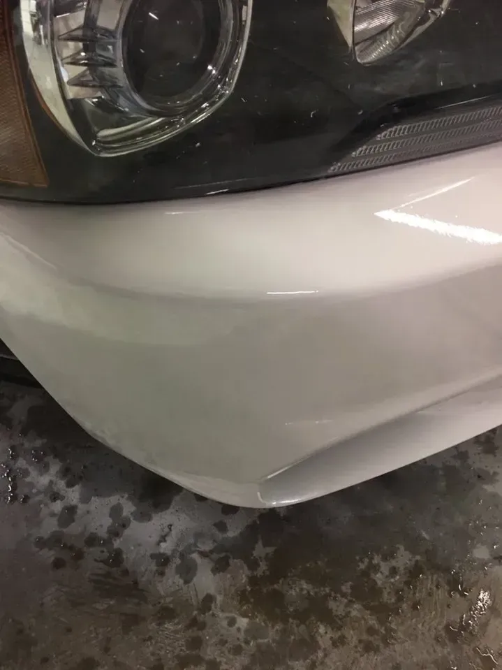 A close up of a white car bumper with a black headlight.