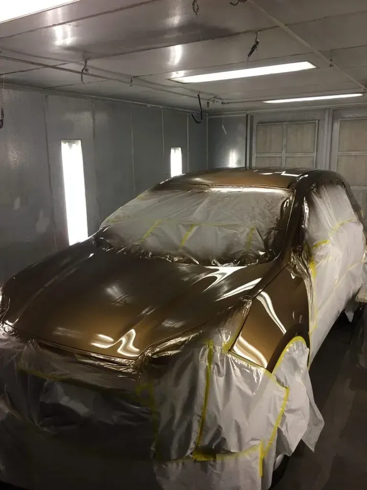 A car is covered in plastic in a paint booth.