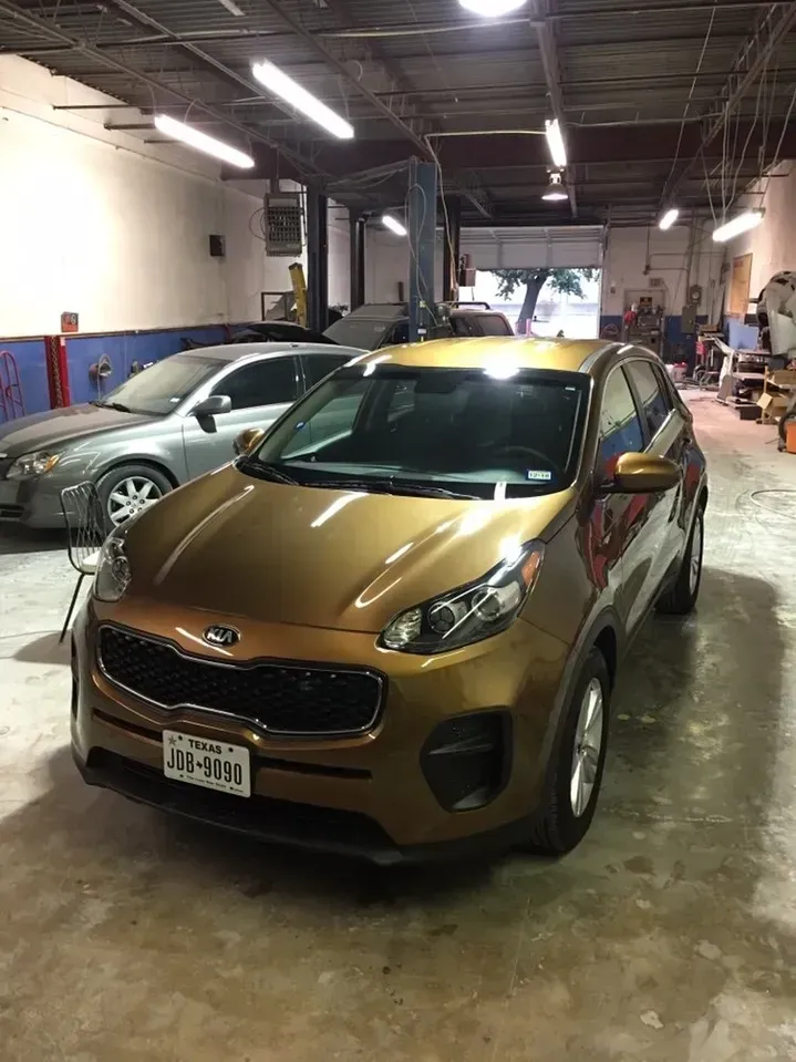 A gold car is parked in a garage next to other cars.