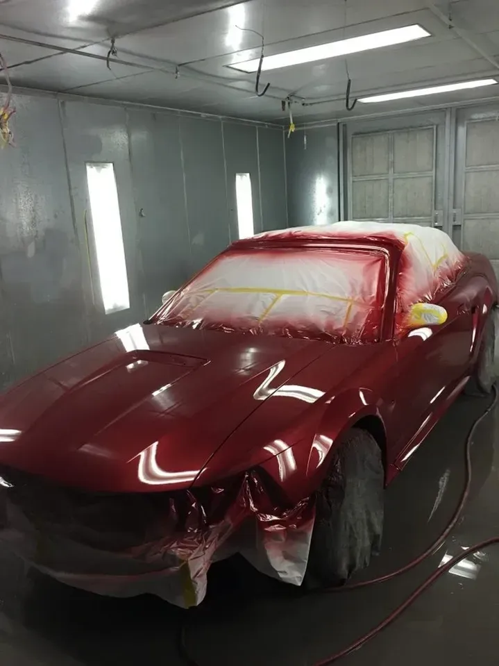 A red car is being painted in a paint booth.