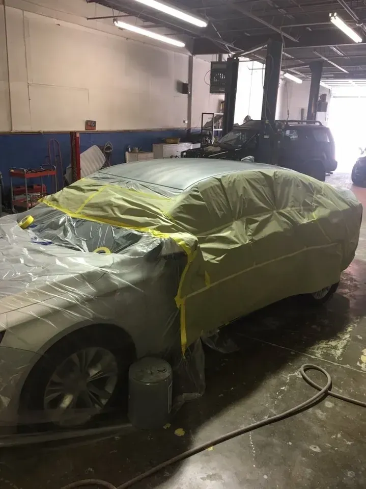 A car is covered in plastic wrap in a garage.