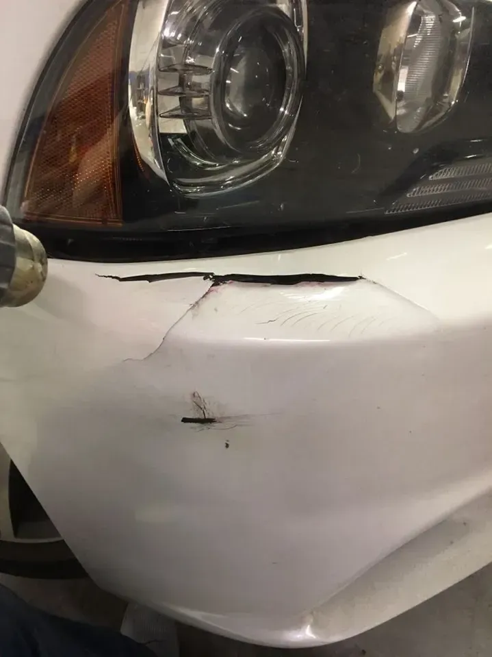 A white car with a damaged bumper and headlight.