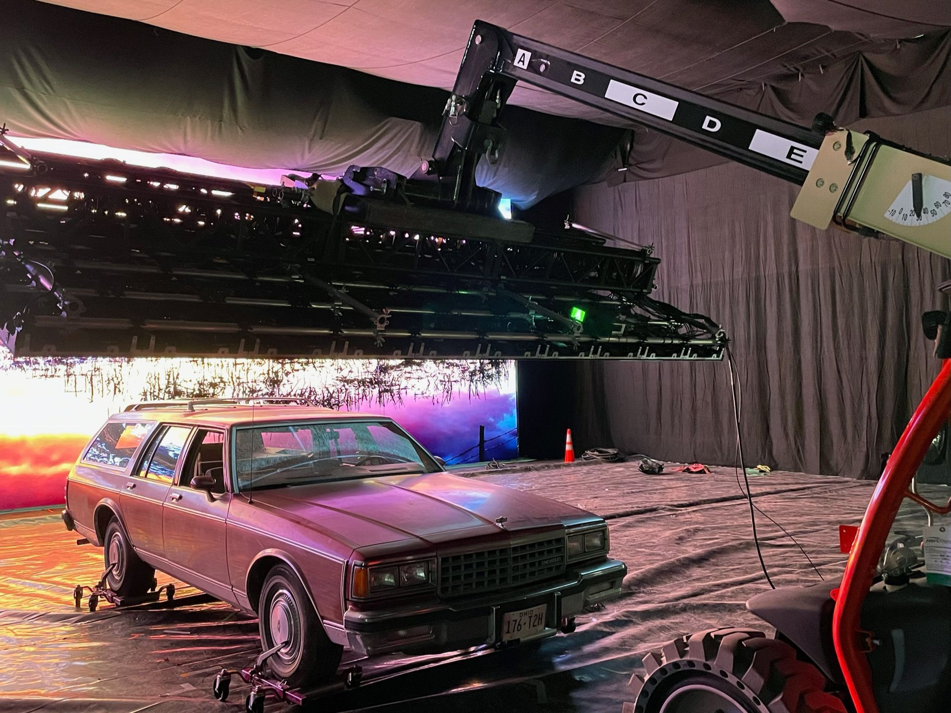 A pink car is being lifted by a crane in a dark room.