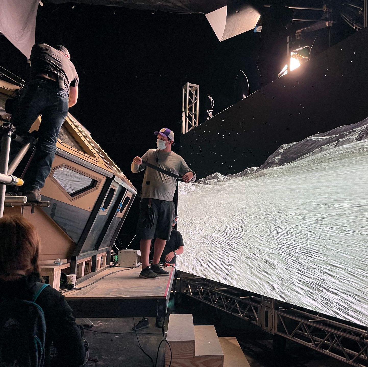 A man in a mask is standing in front of a large screen