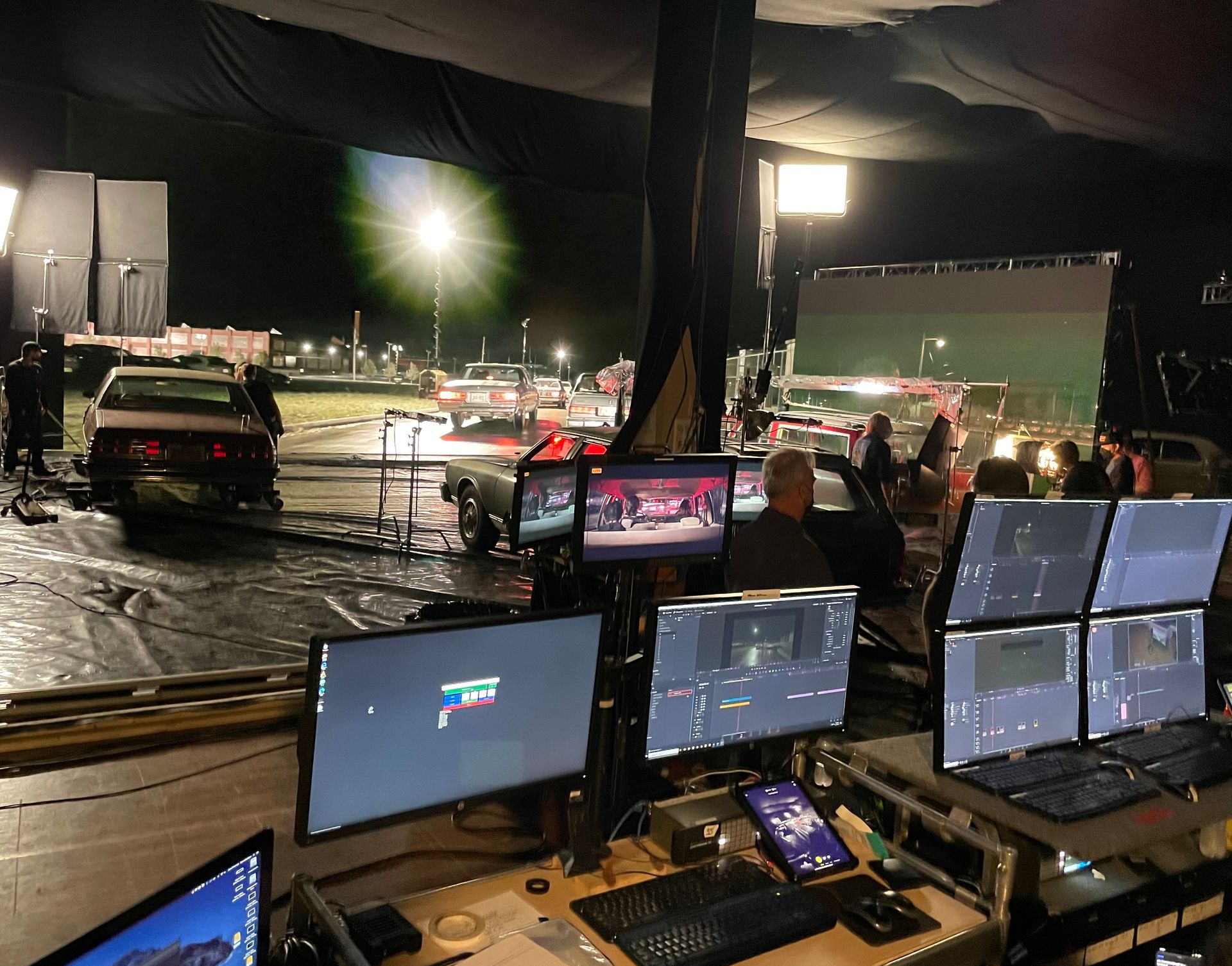Several monitors are sitting on a desk in front of a large screen