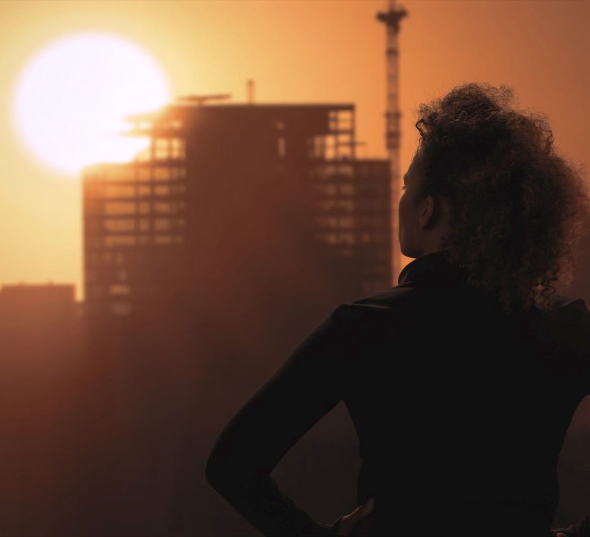 A woman is standing in front of a city skyline at sunset.