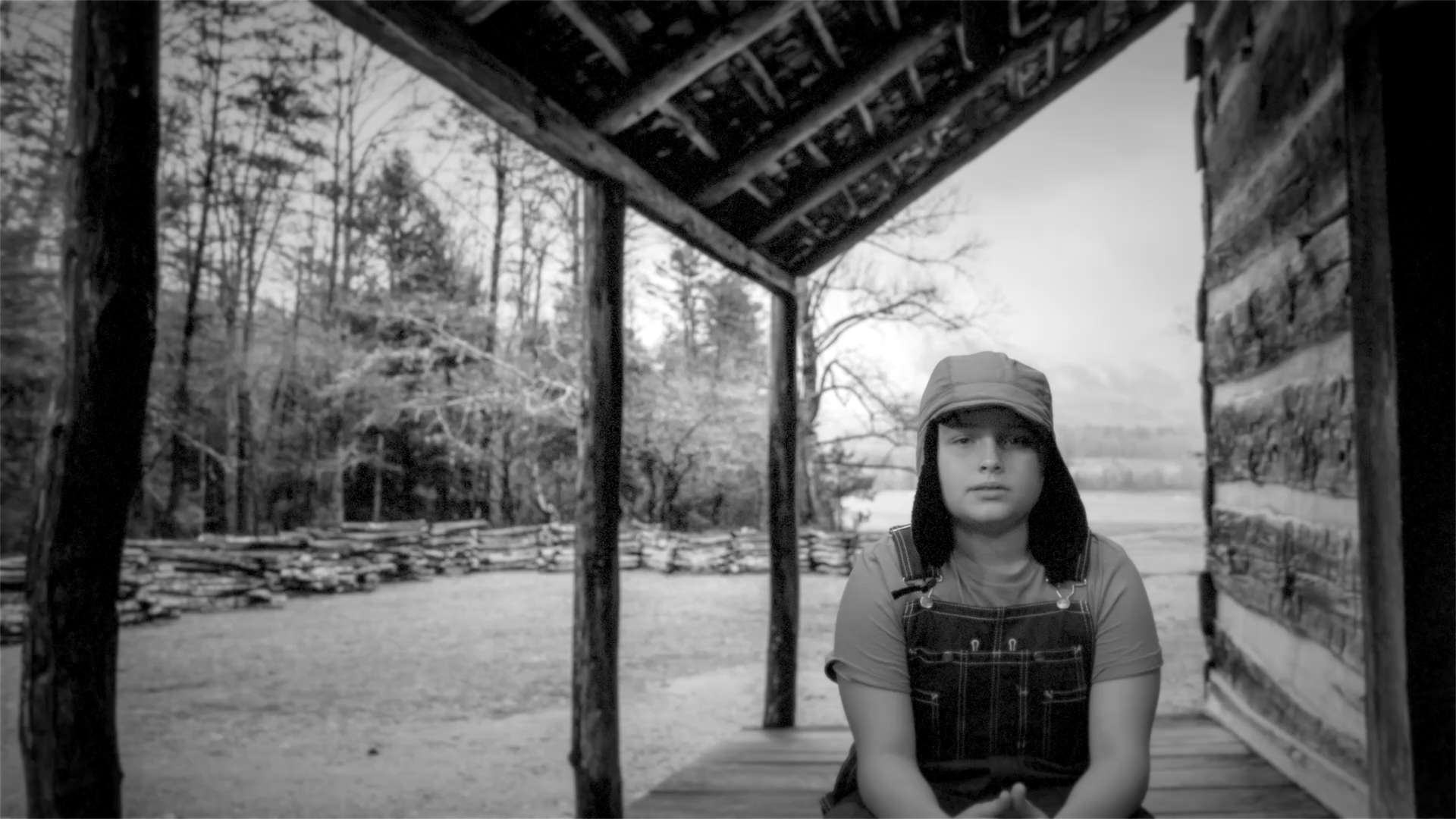 A black and white photo of a woman sitting under a porch.