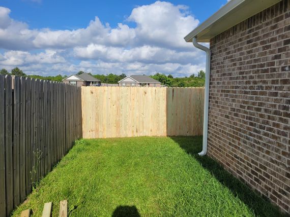 A wooden fence is in the backyard of a brick house.
