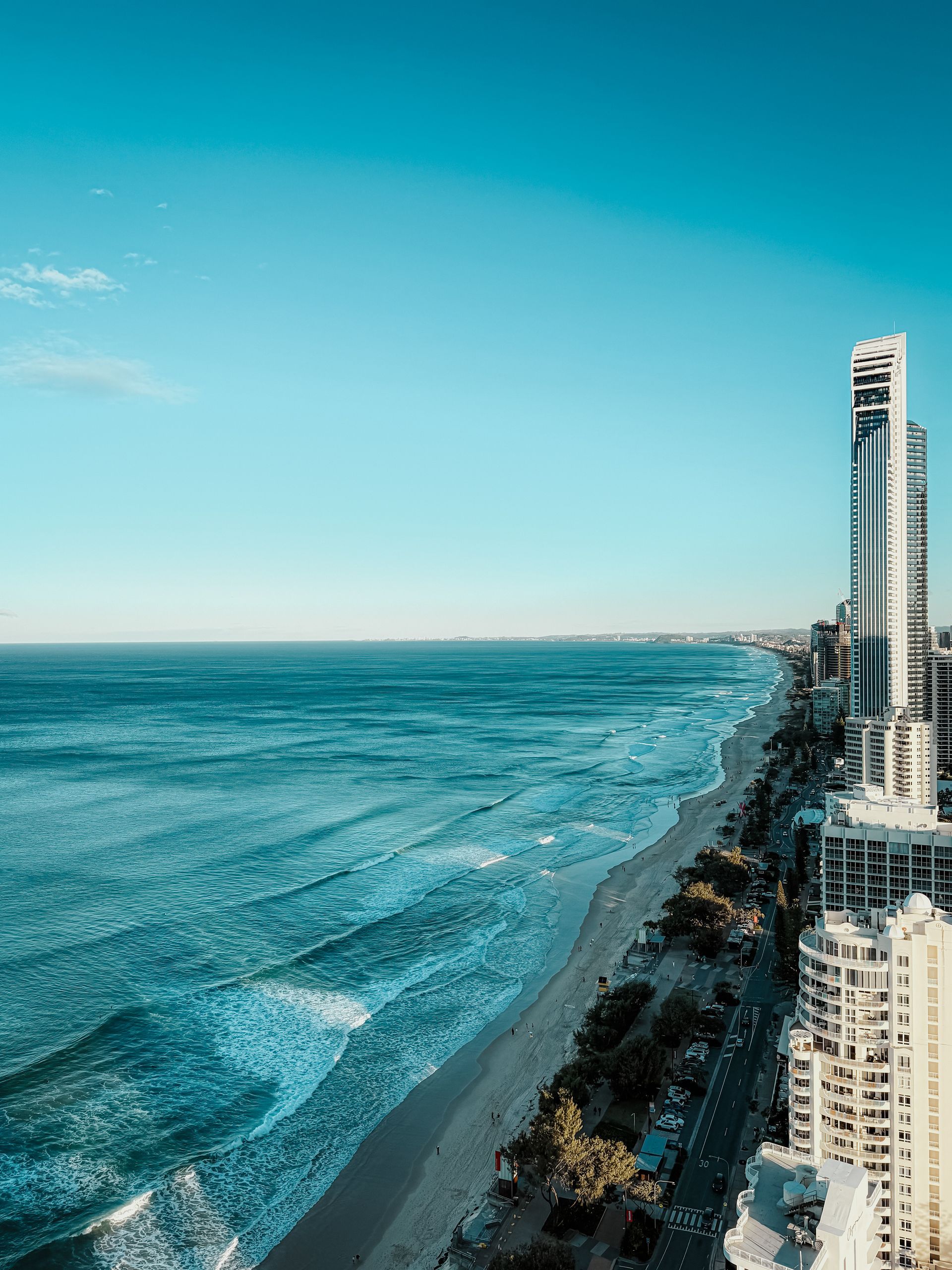Blue ocean and sky meeting a sandy beach lined with buildings.