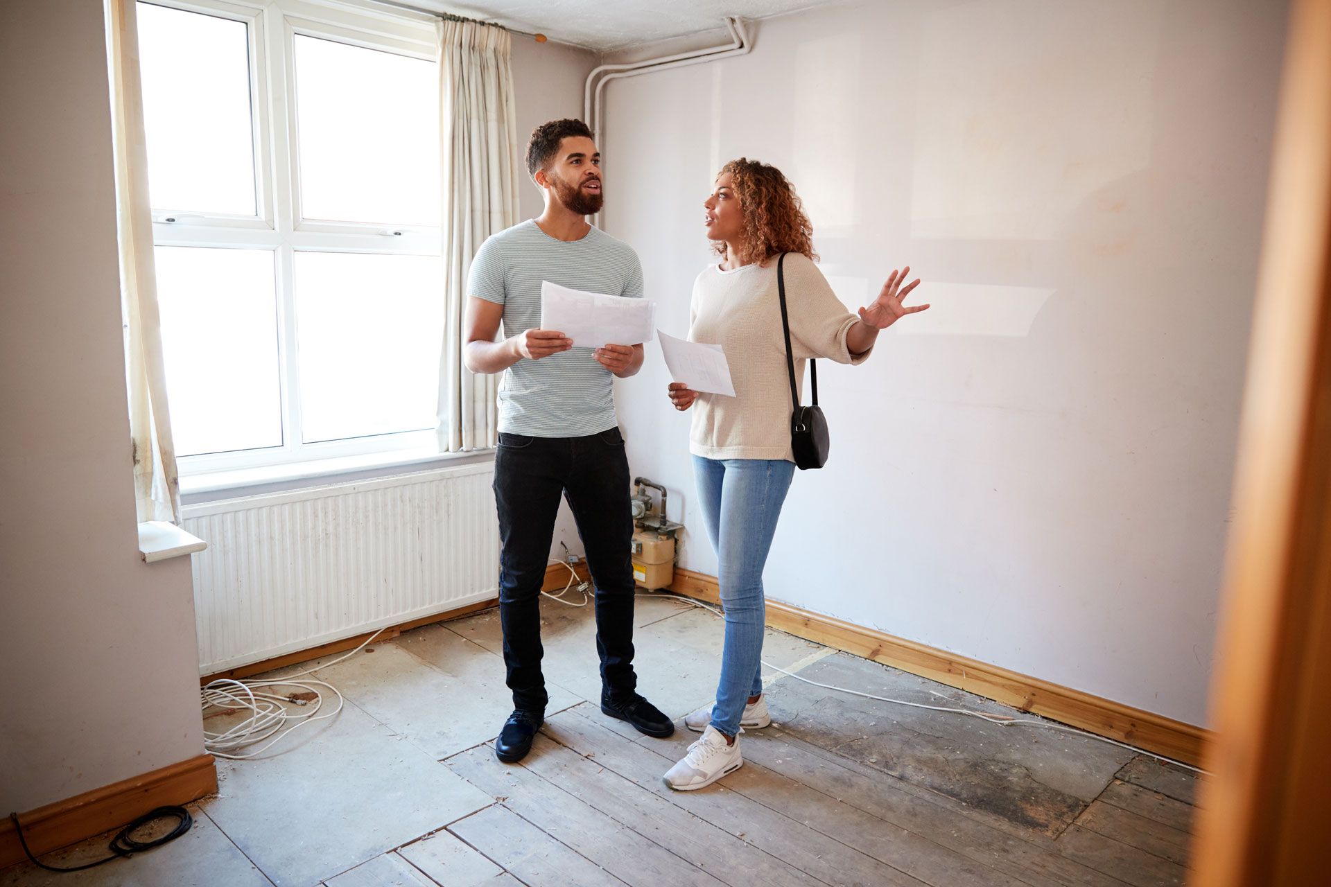 Couple in a bare room, examining papers, discussing potential renovations.
