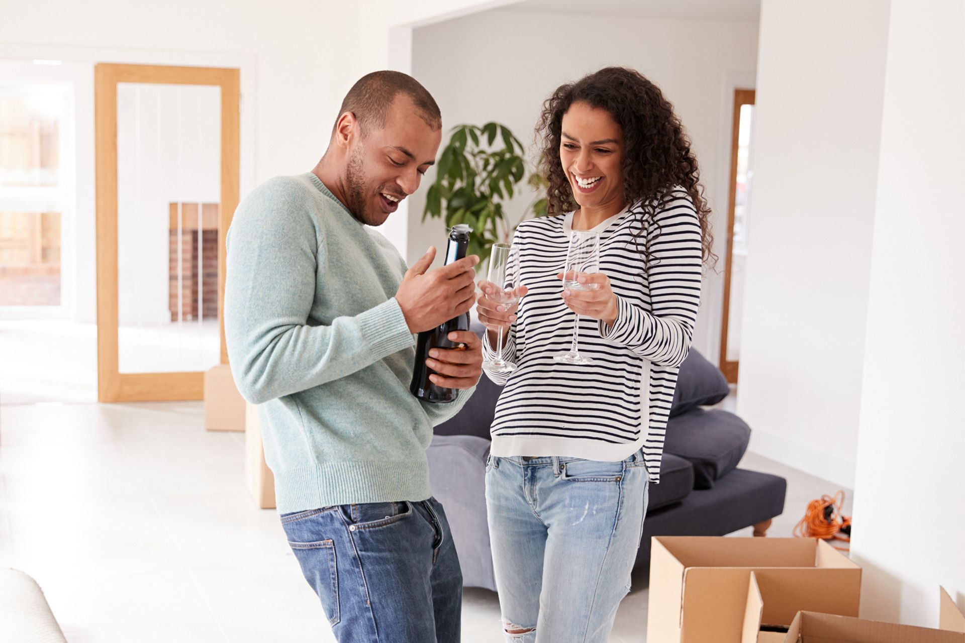 Couple celebrating in new home, man holding bottle, woman with glasses, smiling. Couple celebrating in new home, man holding bottle, woman with glasses, smiling.