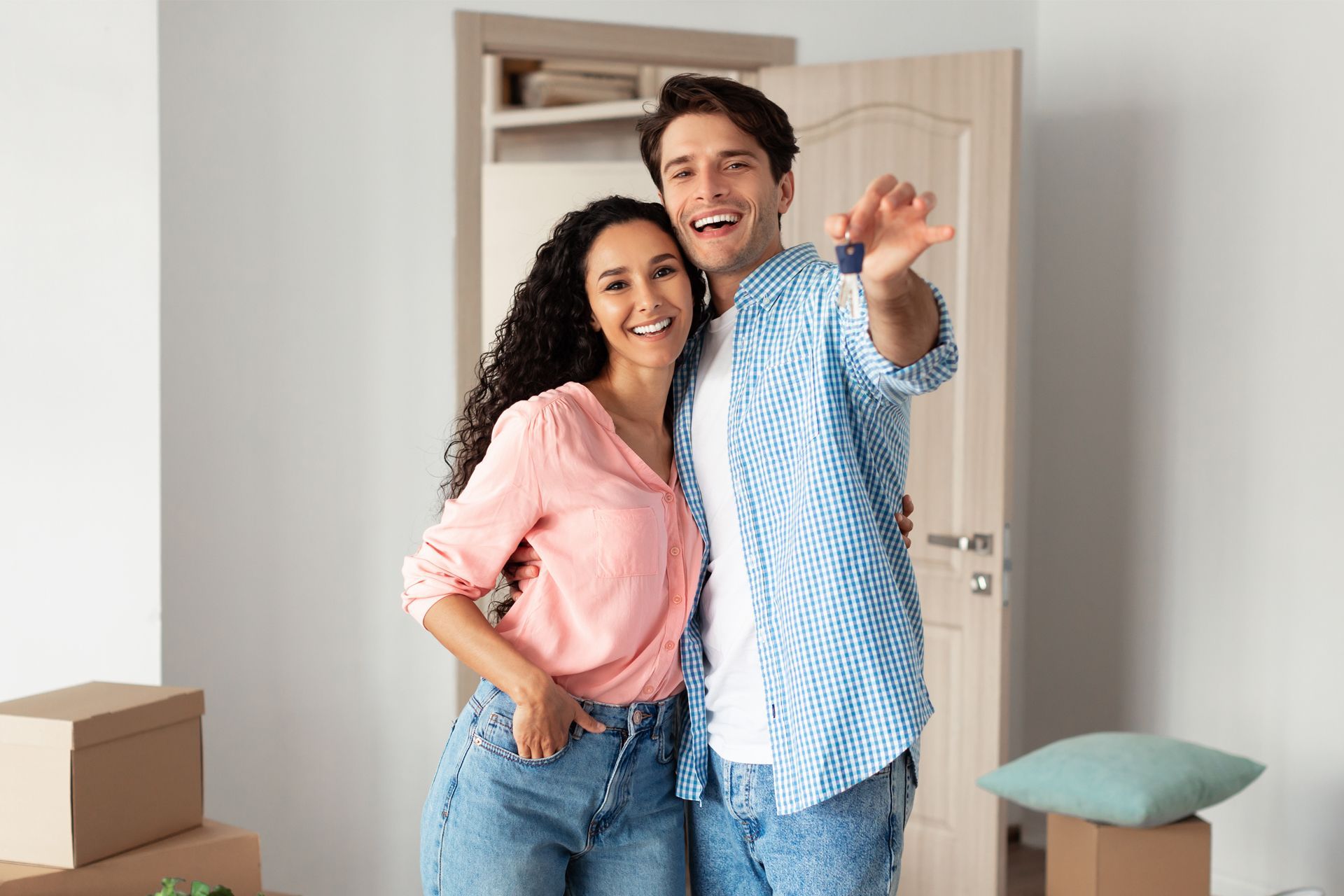 Couple holding keys, smiling in new home, surrounded by boxes.