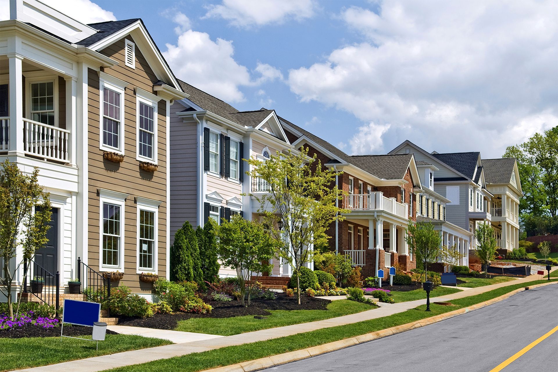 Row of colorful houses with front porches along a street on a sunny day.