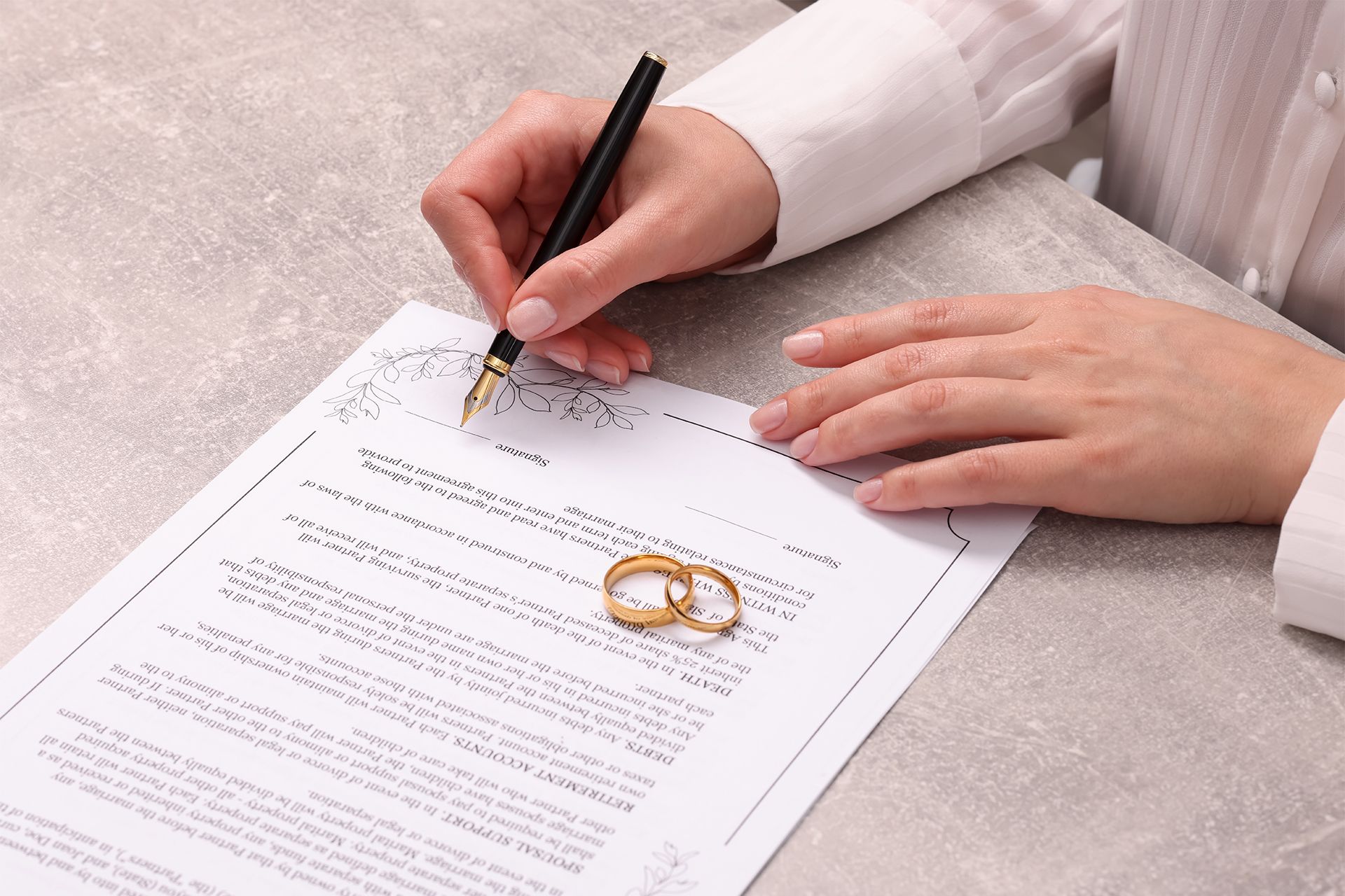 Person signing divorce papers with wedding rings.