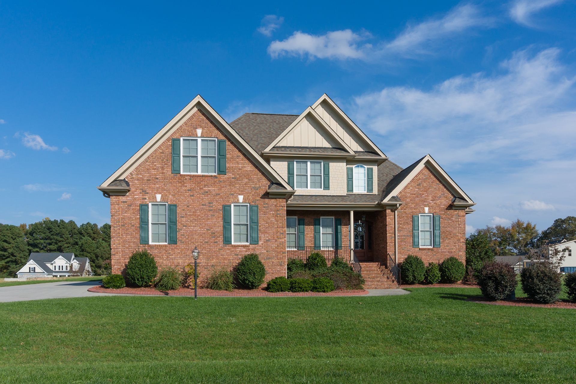 Brick house with green shutters, front lawn, and blue sky.
