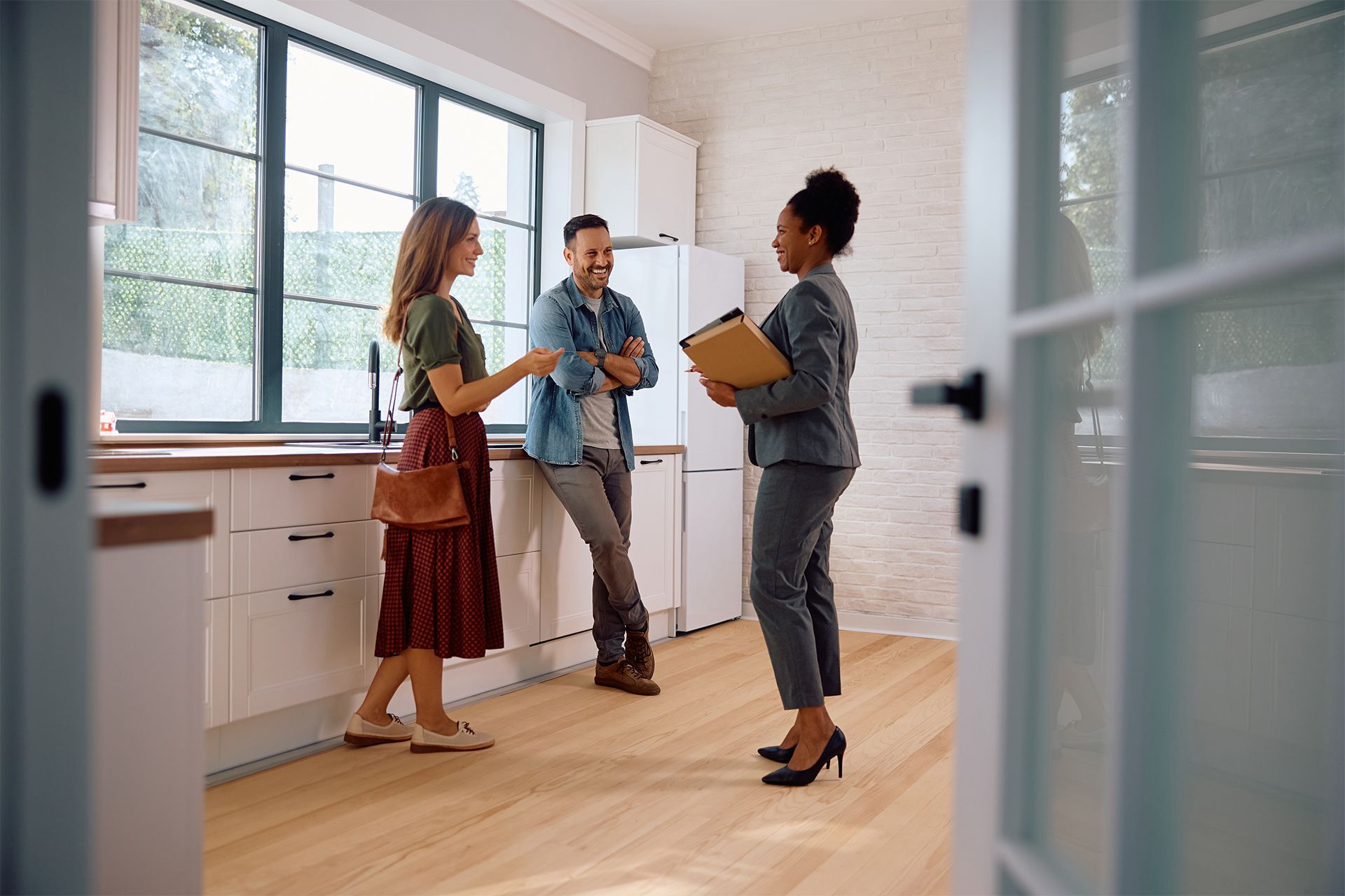 A realtor showing a couple a bright kitchen. The couple is conversing, and the realtor holds a file.