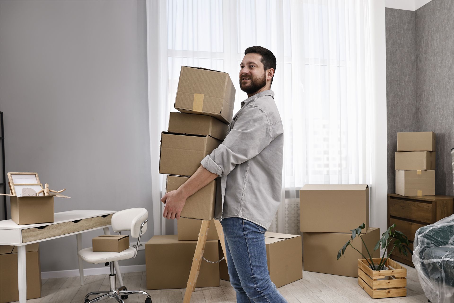 Man carrying a stack of cardboard boxes in a room, preparing to move.