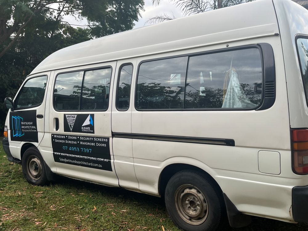 A White Van is Parked in a Grassy Area — Whitsunday Architectural Windows & Doors in Proserpine, QLD