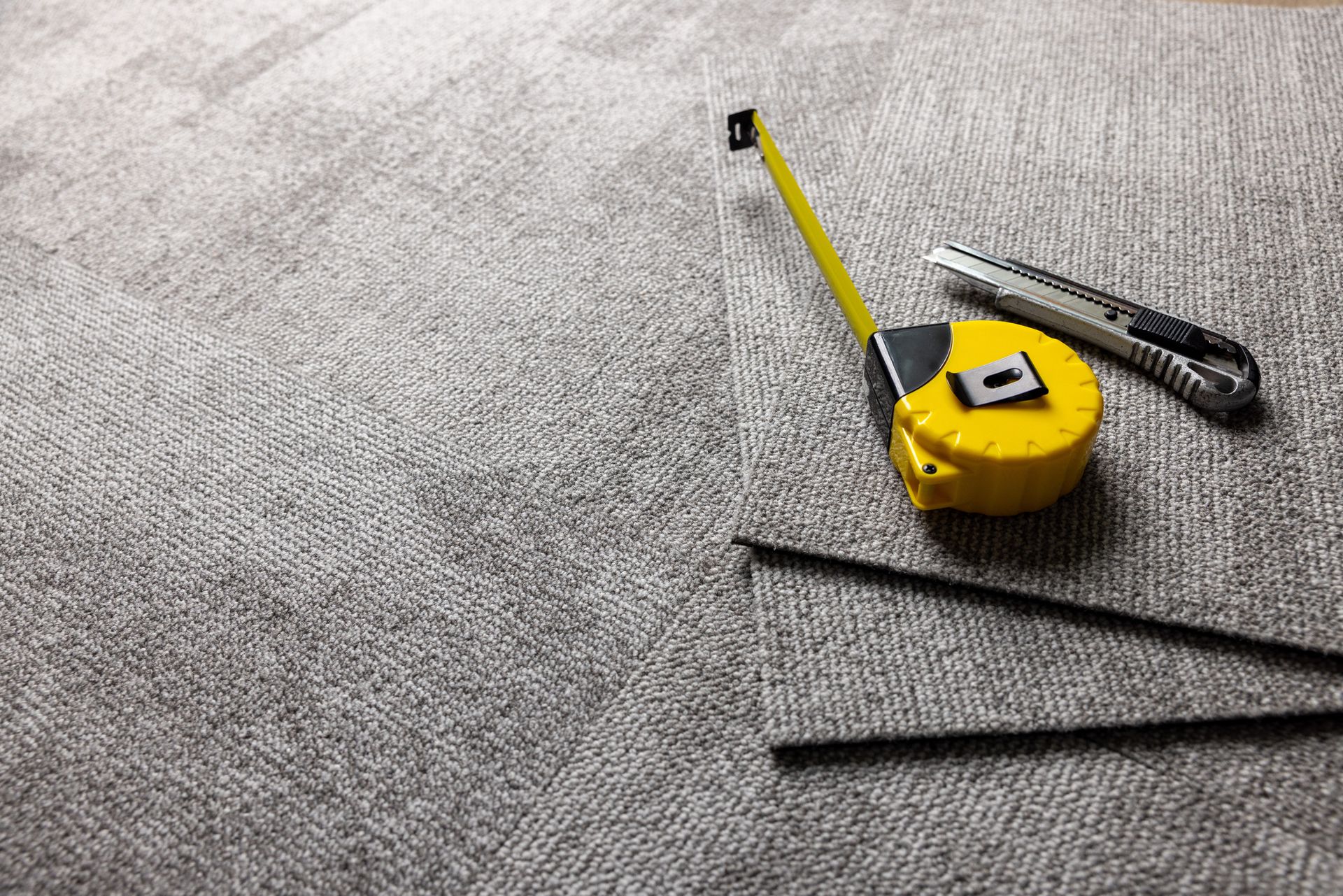 Carpet with a tape measure, utility knife, and black rods.