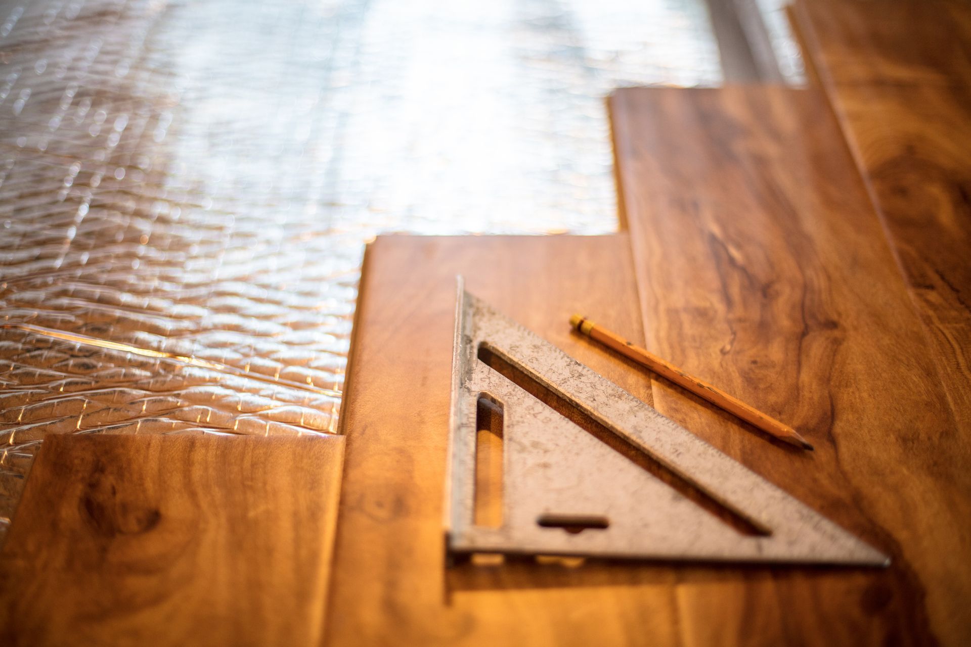 Wooden flooring being installed, with a square, pencil, and planks.