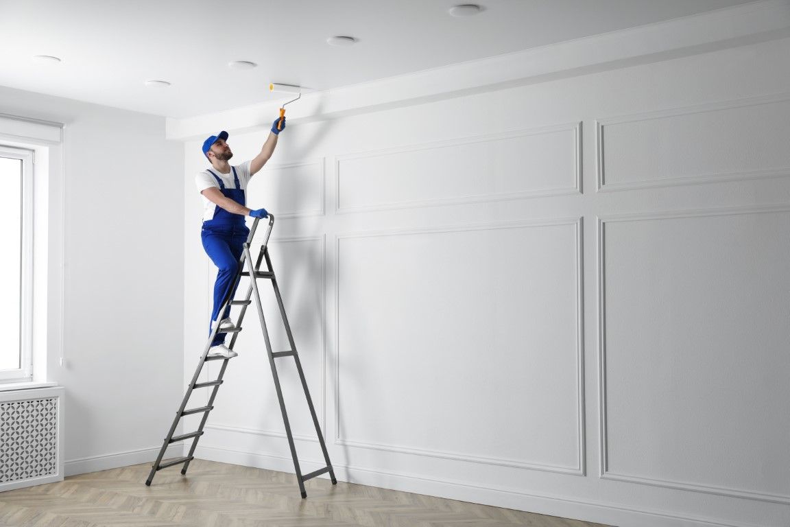A man is standing on a ladder painting a wall.