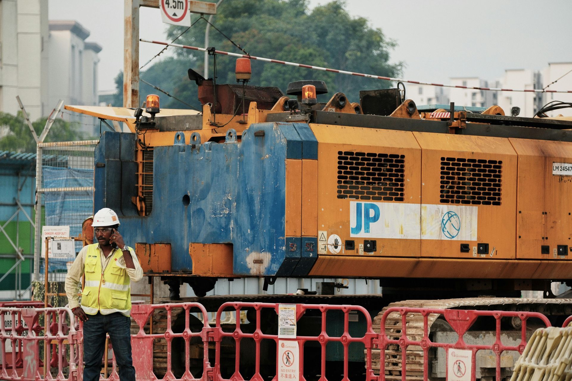 Man with construction safety attire talking on a cellphone at a worksite.