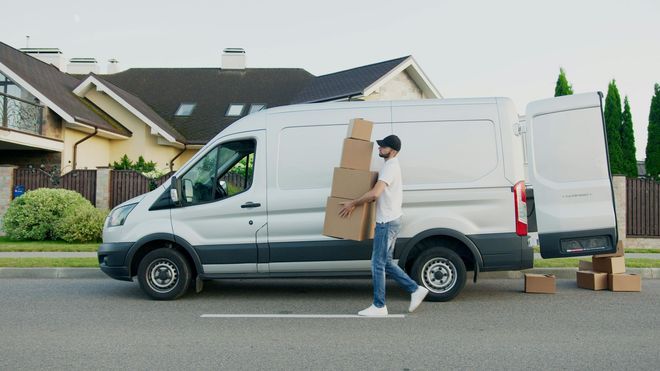 A delivery man is carrying boxes out of a white van.