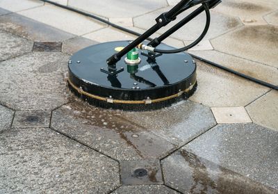 A rotary surface cleaner power washing a paved walkway with hexagonal tiles.