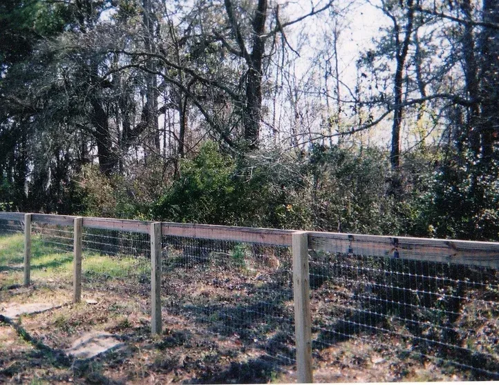 A wooden fence surrounds a field with trees in the background