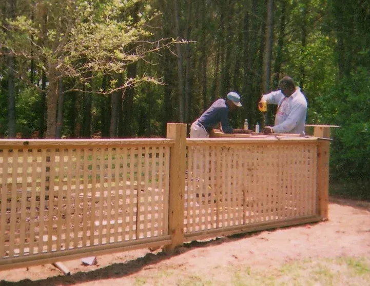 Two men are working on a wooden fence in the woods