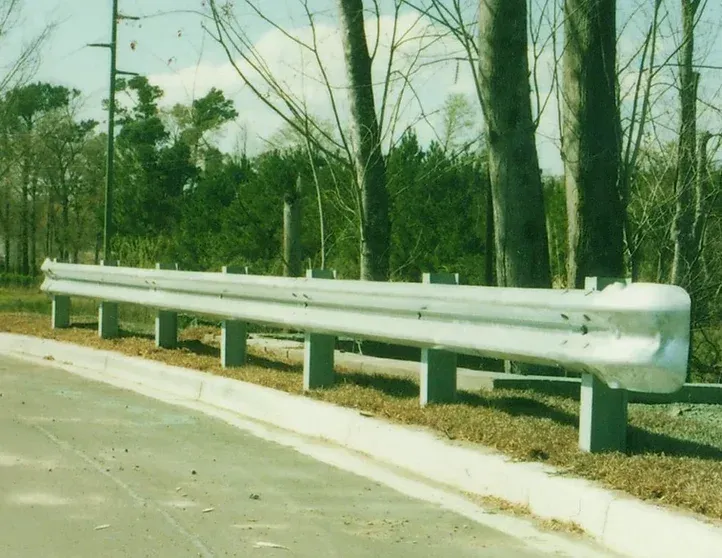 A white railing on the side of a road with trees in the background